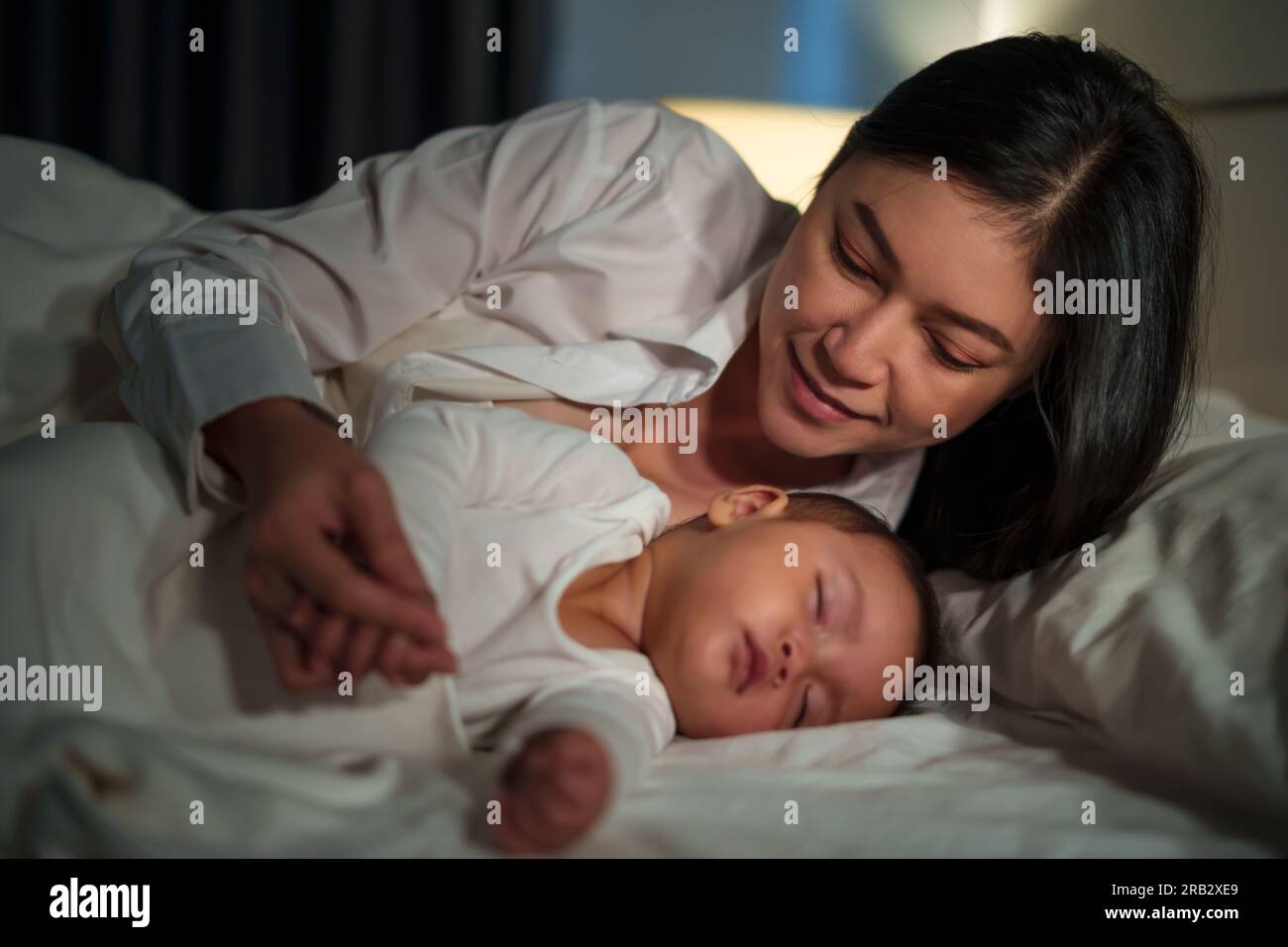happy mother looking with her infant baby sleeping on a bed at night Stock Photo