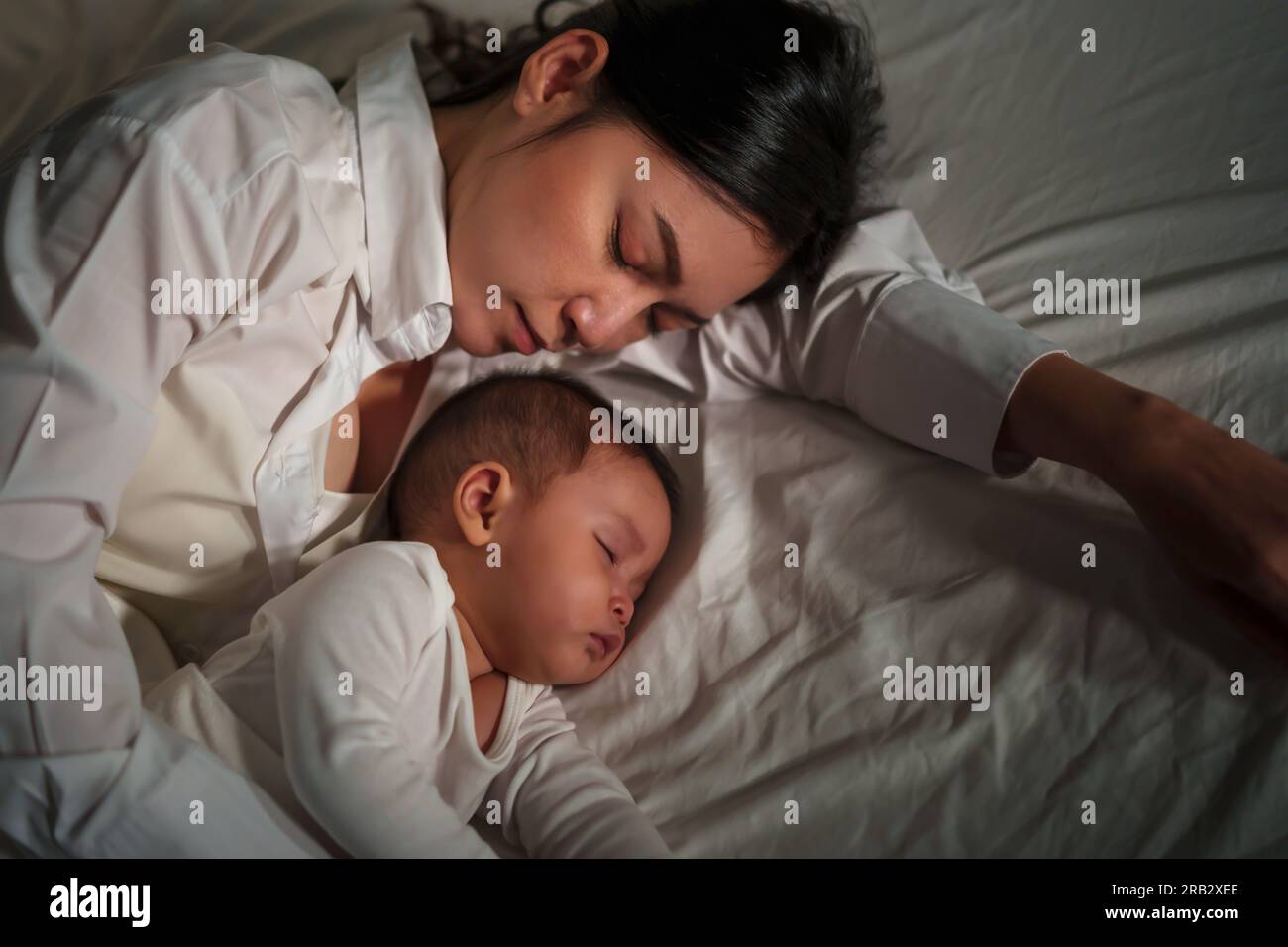 mother embraces the infant baby sleeping together in a bed at night Stock Photo
