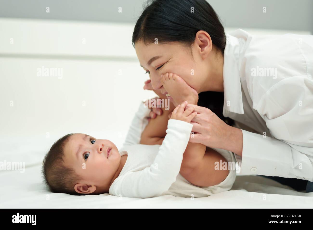 infant baby taps feet on mother's cheek on a bed Stock Photo