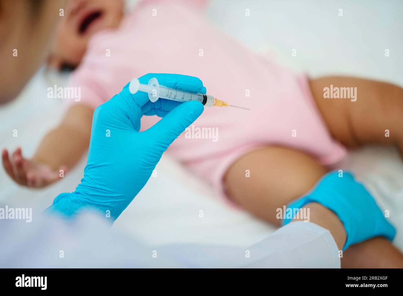 doctor holding syringe and preparing vaccine giving injection to leg of crying infant baby Stock Photo