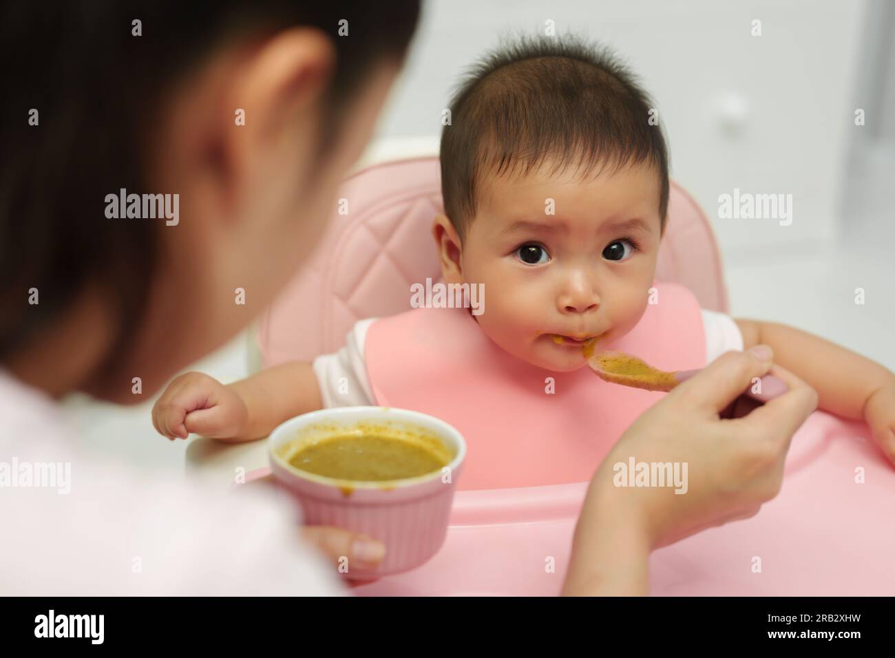 mother feeding food to her infant baby eating with a spoon at home Stock Photo