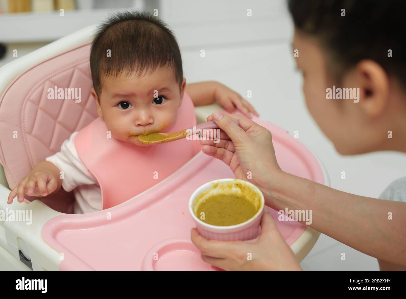 mother feeding food to her infant baby eating with a spoon at home Stock Photo