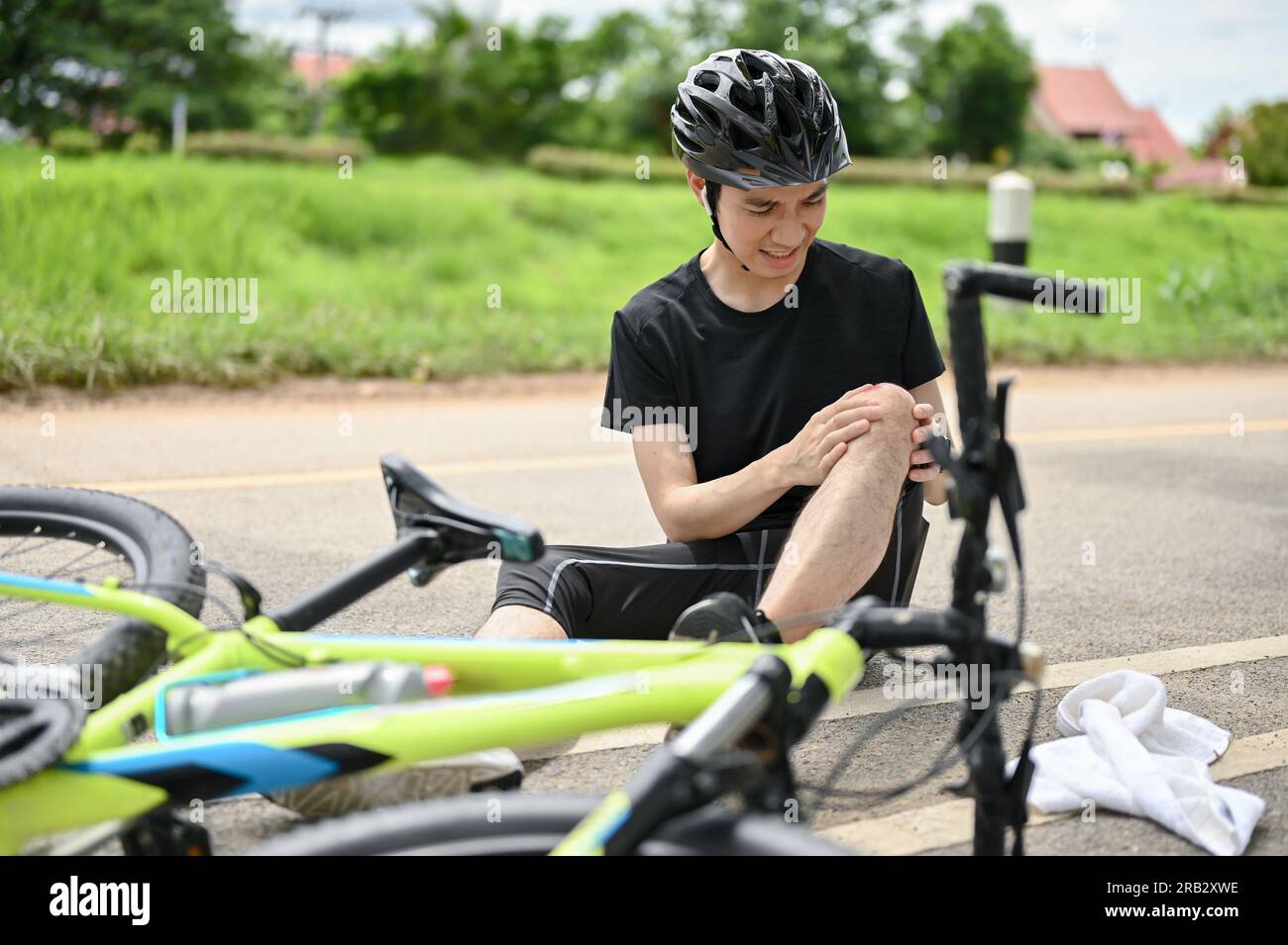 An injured young Asian male cyclist in sportswear and a bike helmet ...