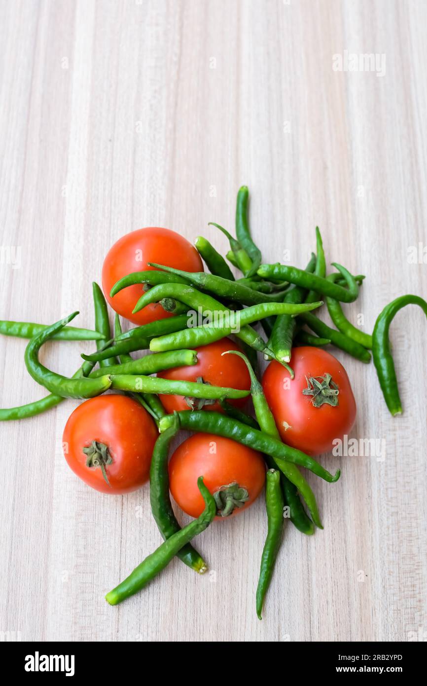 Red tomato and green chili pepper on plain wooden table, green ...