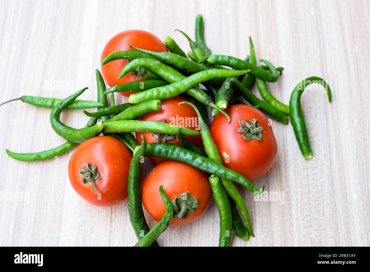 Red tomato and green chili pepper on plain wooden table, green ...