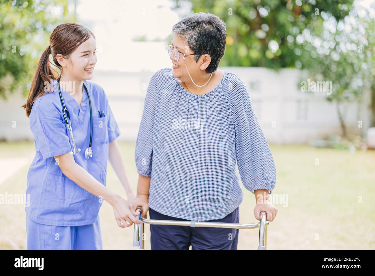 Young nurse helping asian senior woman walking. caregiver assisting old lady patient at nursing home. elder walk with walker at home care. Stock Photo