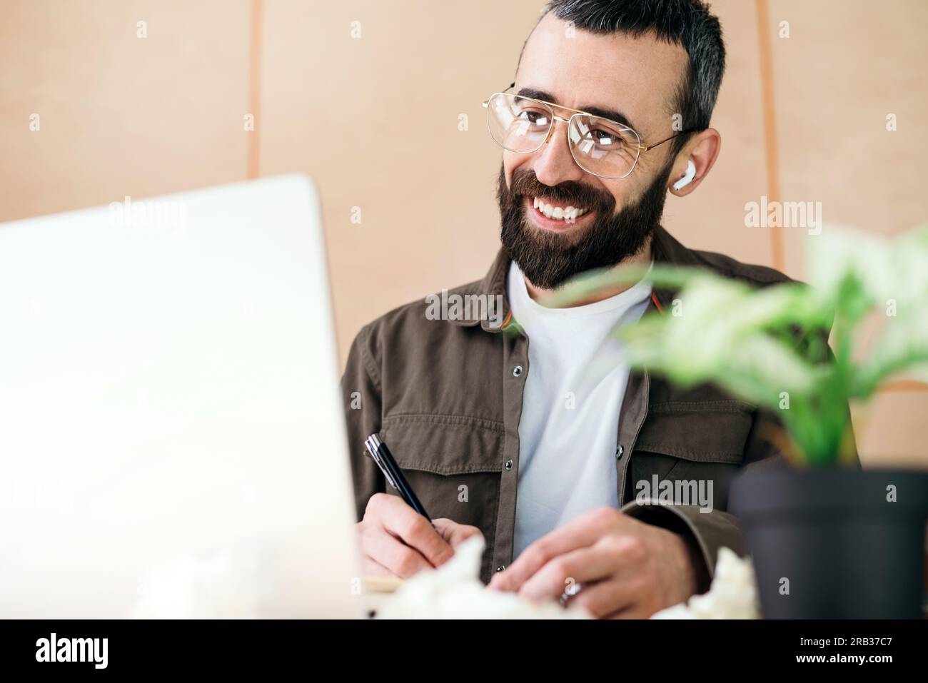 Concentrated man in glasses taking notes writing information from laptop in cafe, cheerful bearded man studying in cafe Stock Photo