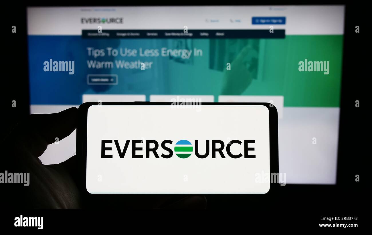 Person holding cellphone with logo of US utility company Eversource Energy on screen in front of business webpage. Focus on phone display. Stock Photo