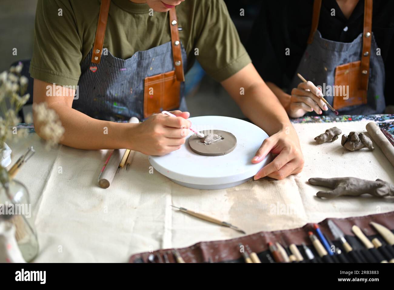 Craftspeople wearing aprons working with raw clay, shaping and decorating pottery in workshop Stock Photo