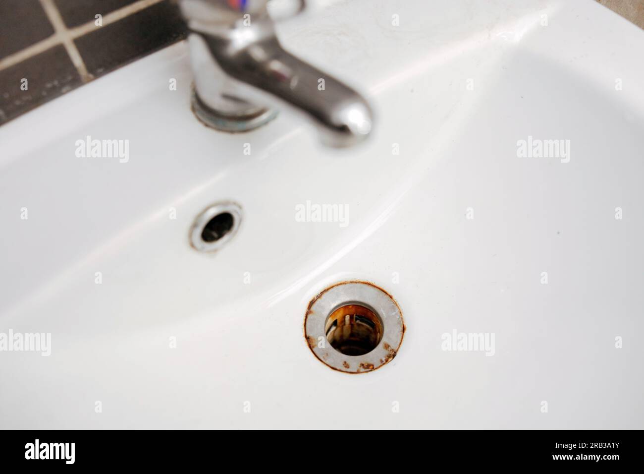 Dirty and rusty washbasin, close up view. Metal drain hole with red