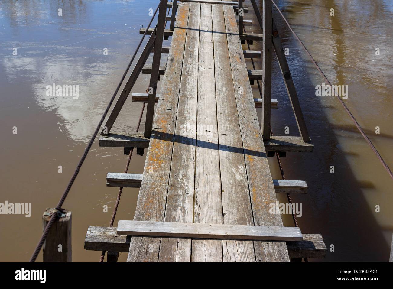 Suspended pedestrian bridge over the river with wooden deck Stock Photo