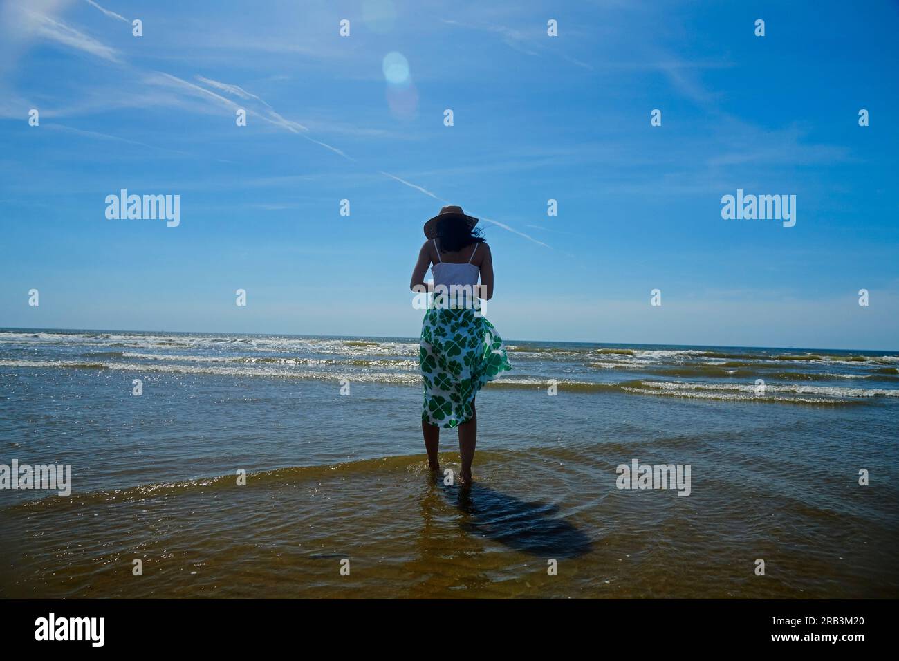 Woman standing in water looking out into the ocean in summer sunshine ...