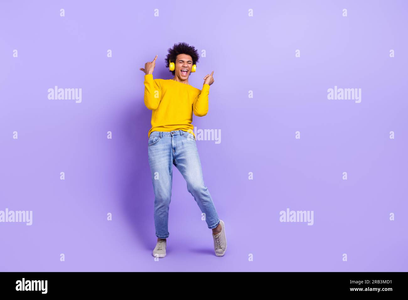Full length portrait of excited young man listen music headphones arms fingers show shaka sign empty space isolated on purple color background Stock Photo