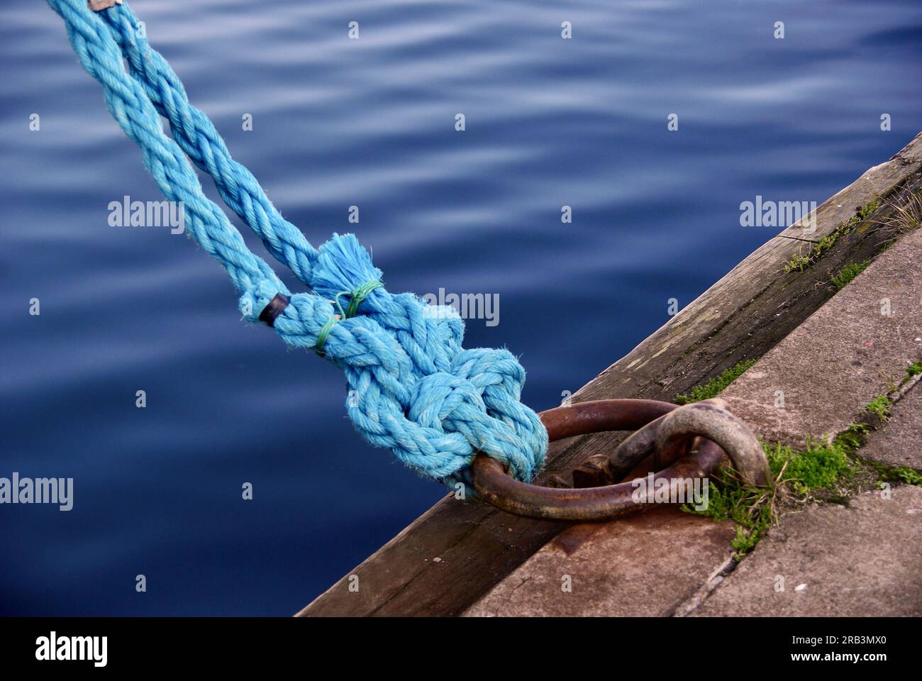 Two blue ropes with a lot of knots around a mooring ring in a harbor. Stock Photo