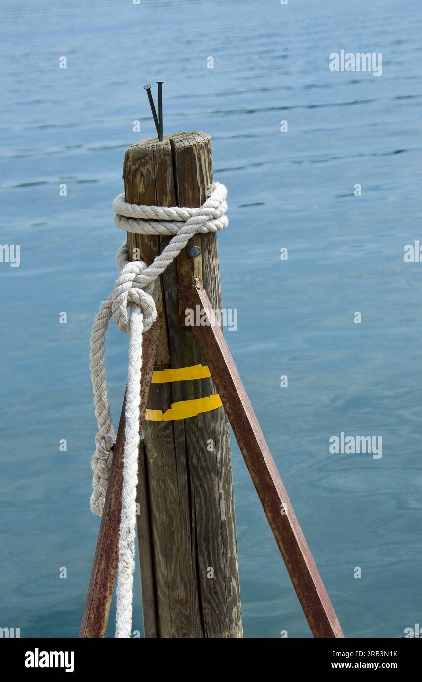 Wooden stake with mooring ropes on the boat jetty in a harbor in  summer. Stock Photo
