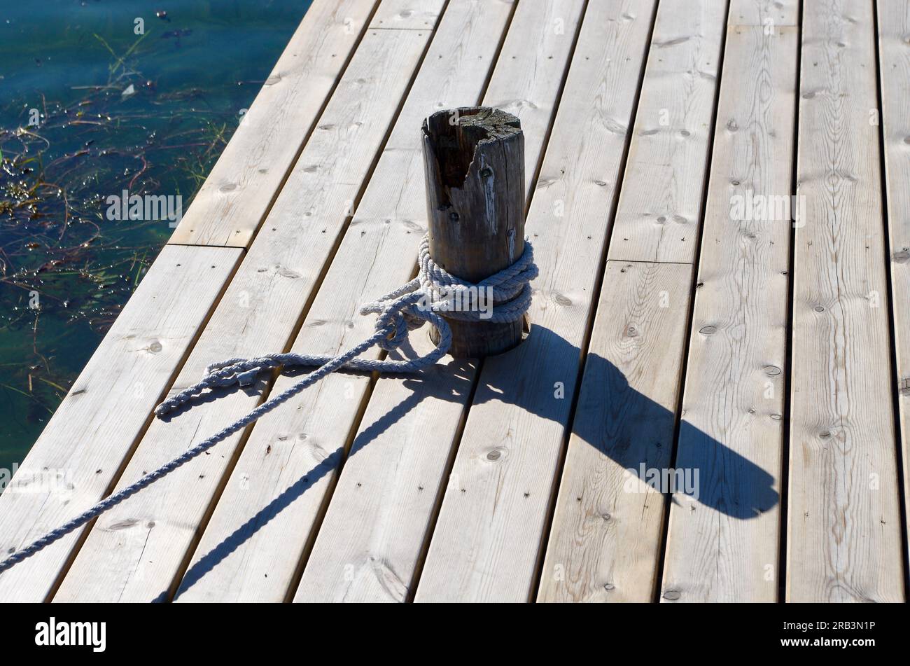 Wooden pier with a wooden pole bollard and tied ropes. Stock Photo