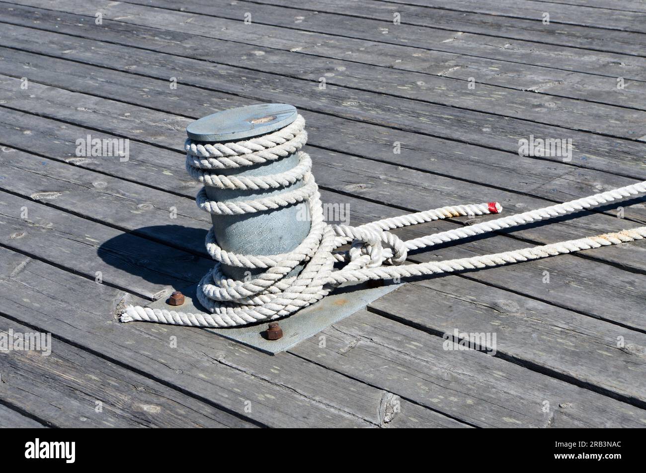 Bollard with mooring rope on wooden quay in a harbor. Stock Photo