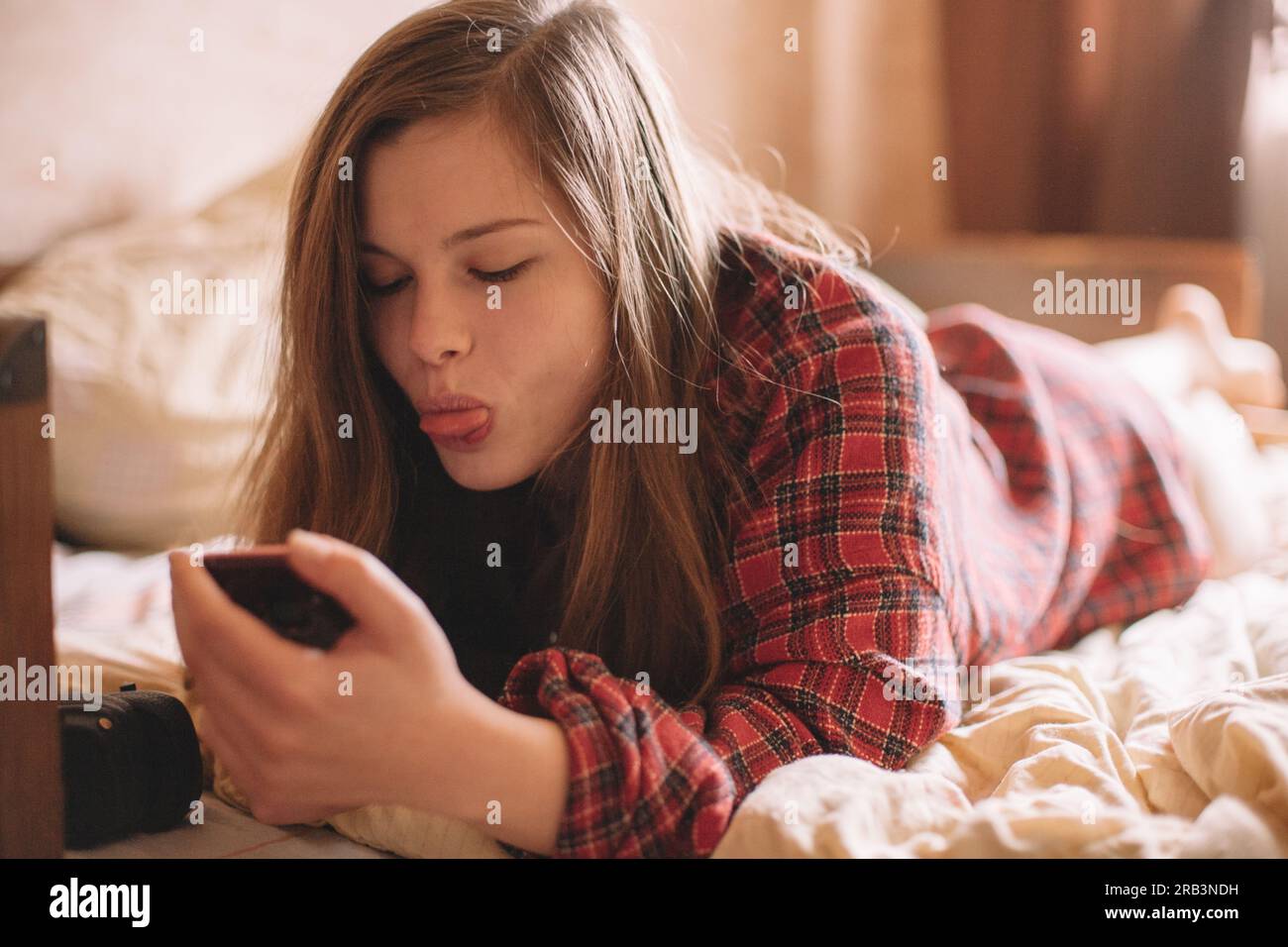 Teenage girl sticking tongue while using smart phone lying on bed Stock Photo