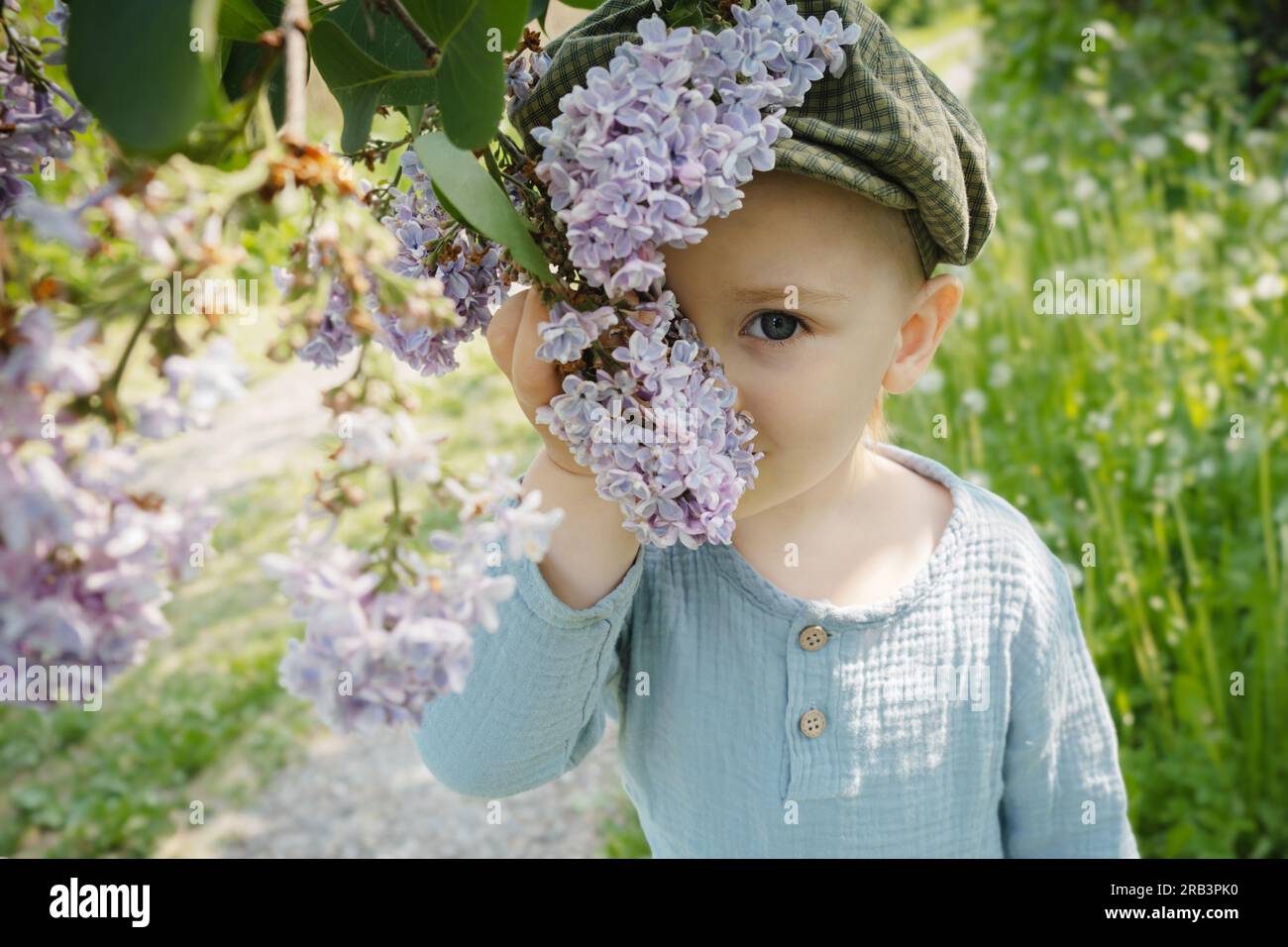Spring portrait of cute toddler boy with blooming lilac branch. Stock Photo