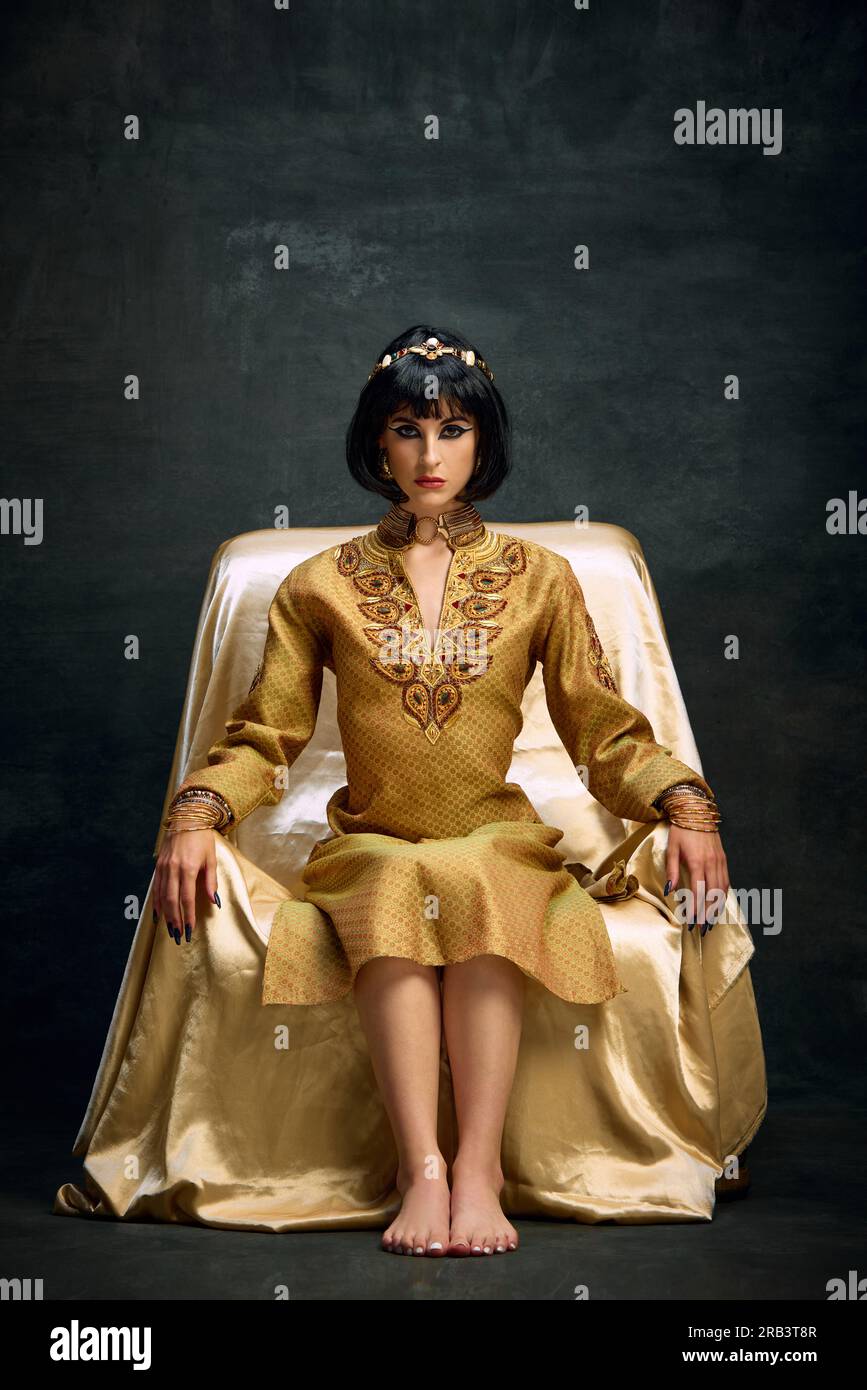 Noble look. Portrait of beautiful young woman in image of Cleopatra, queen in elegant gold dress sitting against dark vintage background Stock Photo - Alamy Noble look. Portrait of beautiful young woman in image of Cleopatra, queen in elegant gold dress sitting against dark vintage background Stock Photo - Alamy