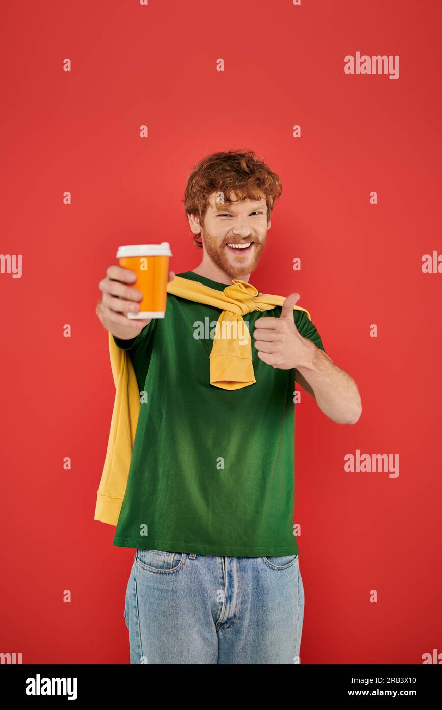 morning coffee, energy, like, redhead man with beard and curly hair holding paper cup on coral background, vibrant colors, male fashion, takeaway drin Stock Photo