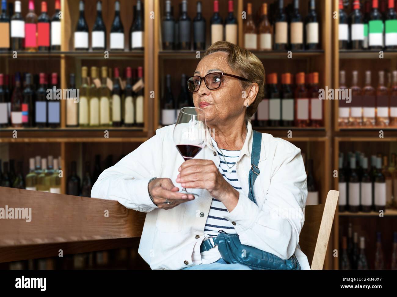Short hair elderly woman wearing sunglasses tasting red wine in a wine boutique. Stock Photo