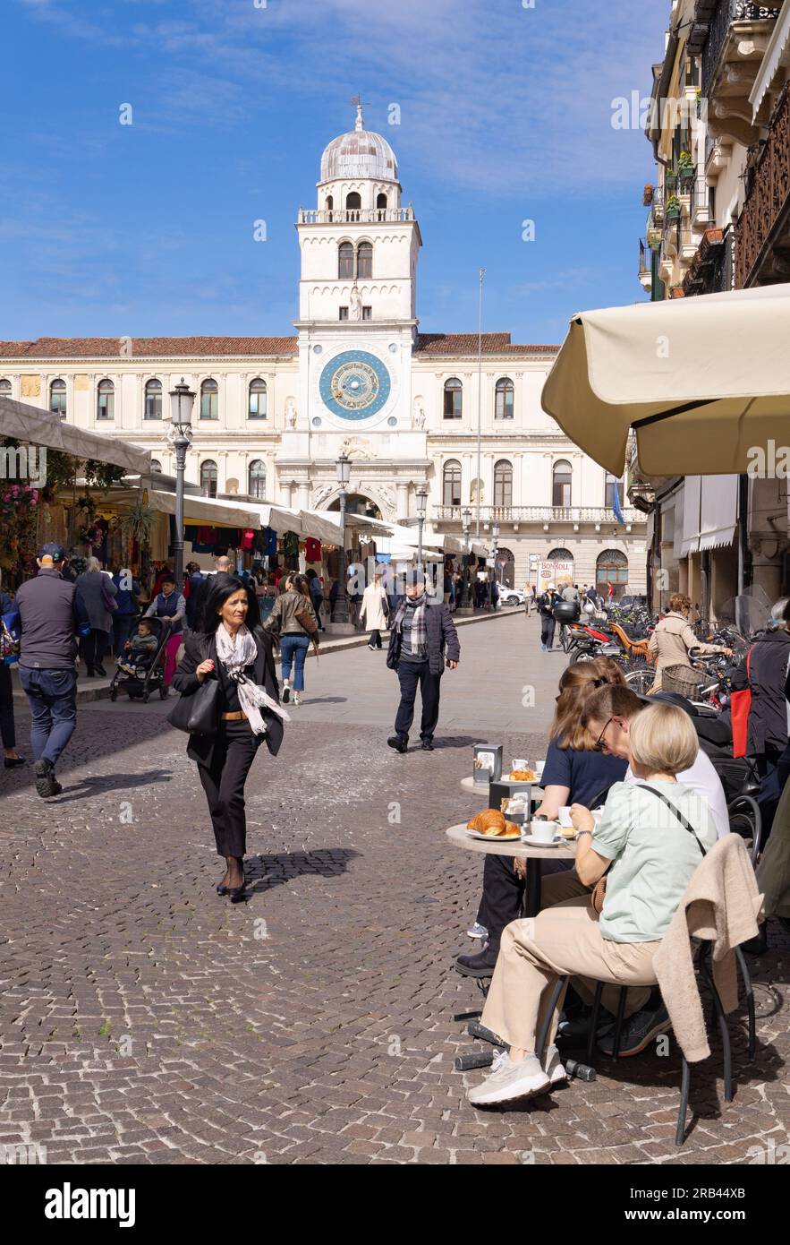 People in a street cafe, Street view in Piazza dei Signori square, with its medieval clock on a sunny spring day, Padua Veneto Italy Europe. Travel Stock Photo