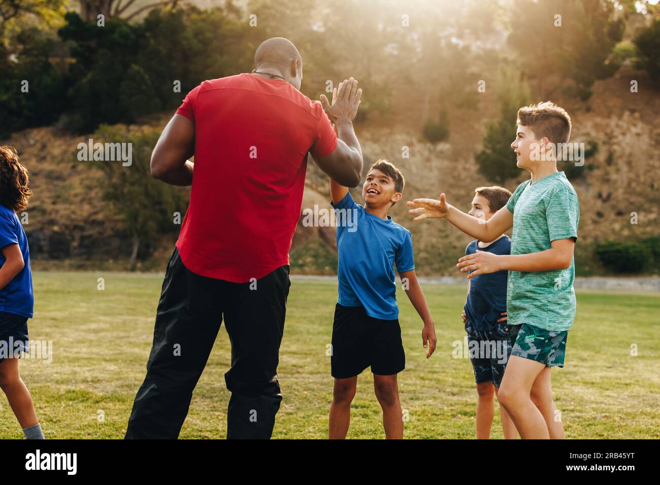 Rugby coach doing a high five with his elementary school team. Sports instructor celebrating with his students in a field. Student mentorship and deve Stock Photo