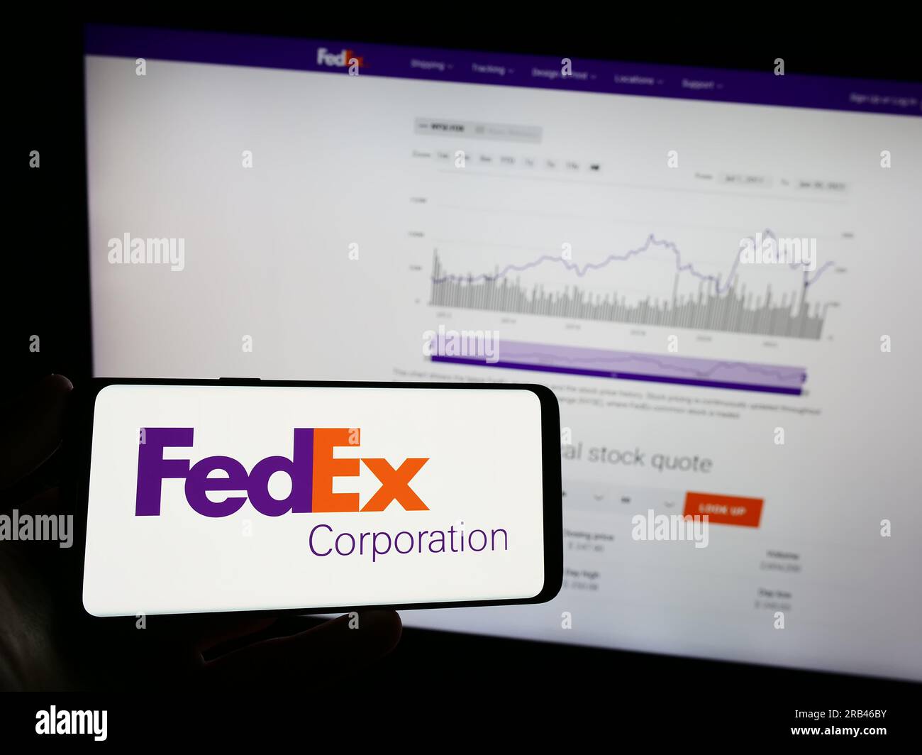 Person holding mobile phone with logo of American logistics company FedEx Corporation on screen in front of web page. Focus on phone display. Stock Photo