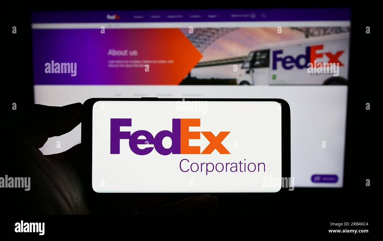 Person holding smartphone with logo of US logistics company FedEx Corporation on screen in front of website. Focus on phone display. Stock Photo