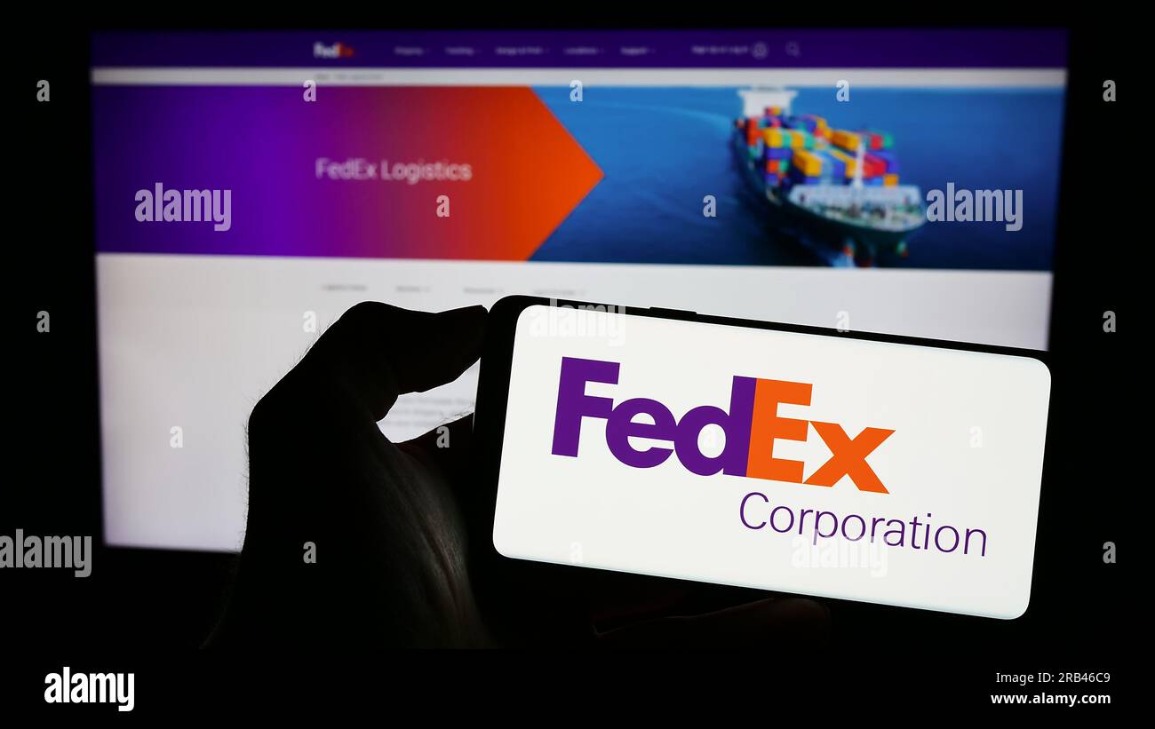Person holding cellphone with logo of US logistics company FedEx Corporation on screen in front of business webpage. Focus on phone display. Stock Photo