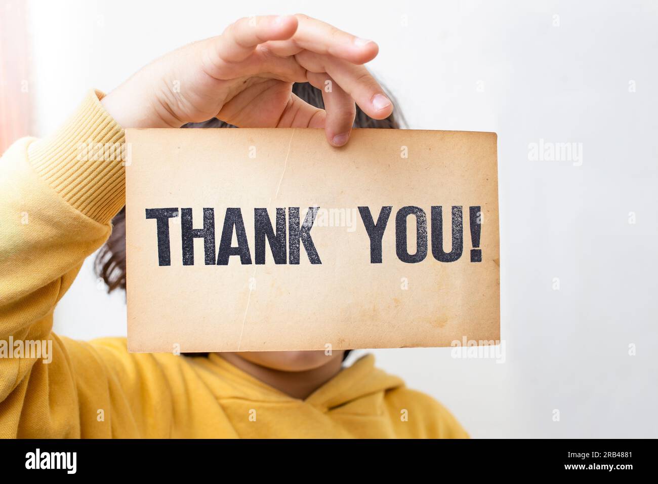 Caucasian male child holding a piece of vintage yellowed paper with Thank you! written with stamp letters. Stock Photo