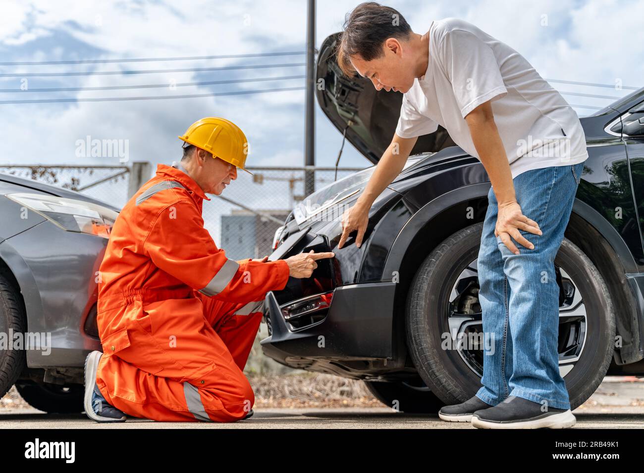 A man pointing out the scratches on his car from the car accident to the car insurance mechanic wearing yellow hardhat and orange jumpsuit or agent at Stock Photo