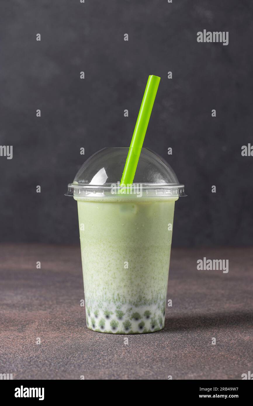Takea way glass of iced matcha green tea latte with bubble on dark gray