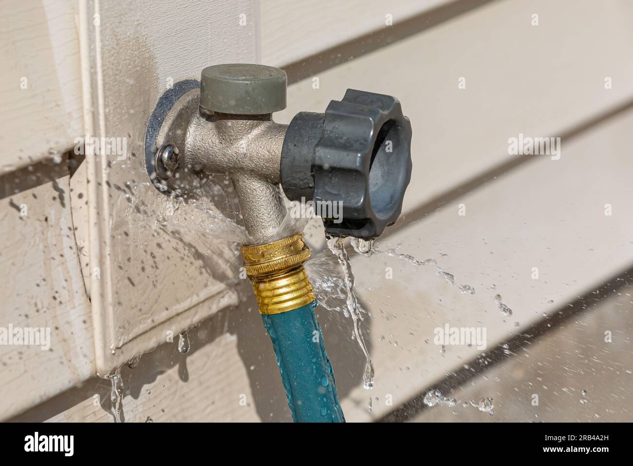 Water leaking from garden hose on outdoor spigot. Water waste, conservation and home repair concept. Stock Photo