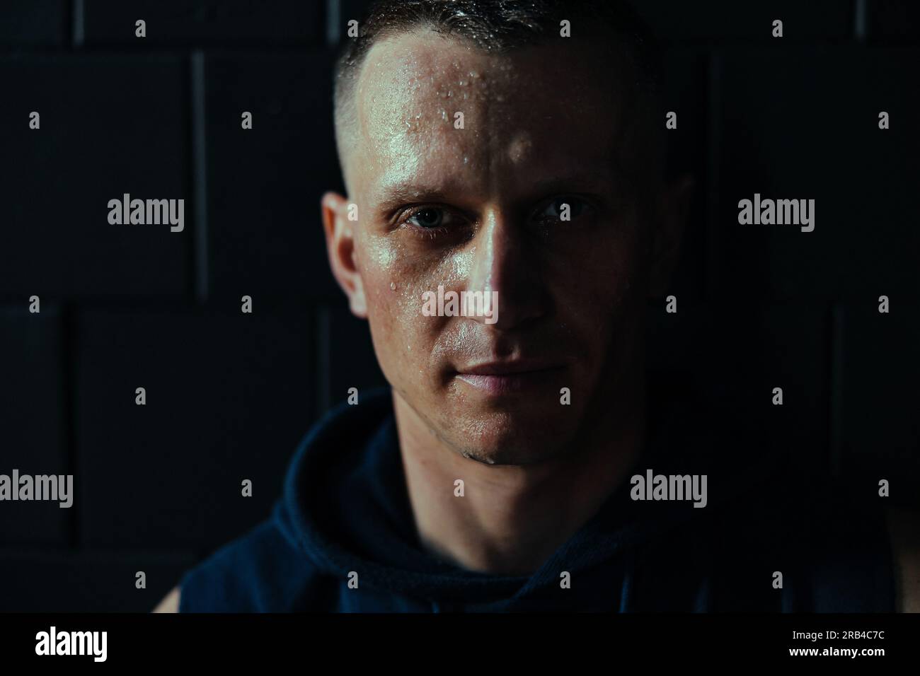 Split portrait with light and shadow of middle age tired athlete man with drops of perspiration on his face after exercising in gym. Stock Photo