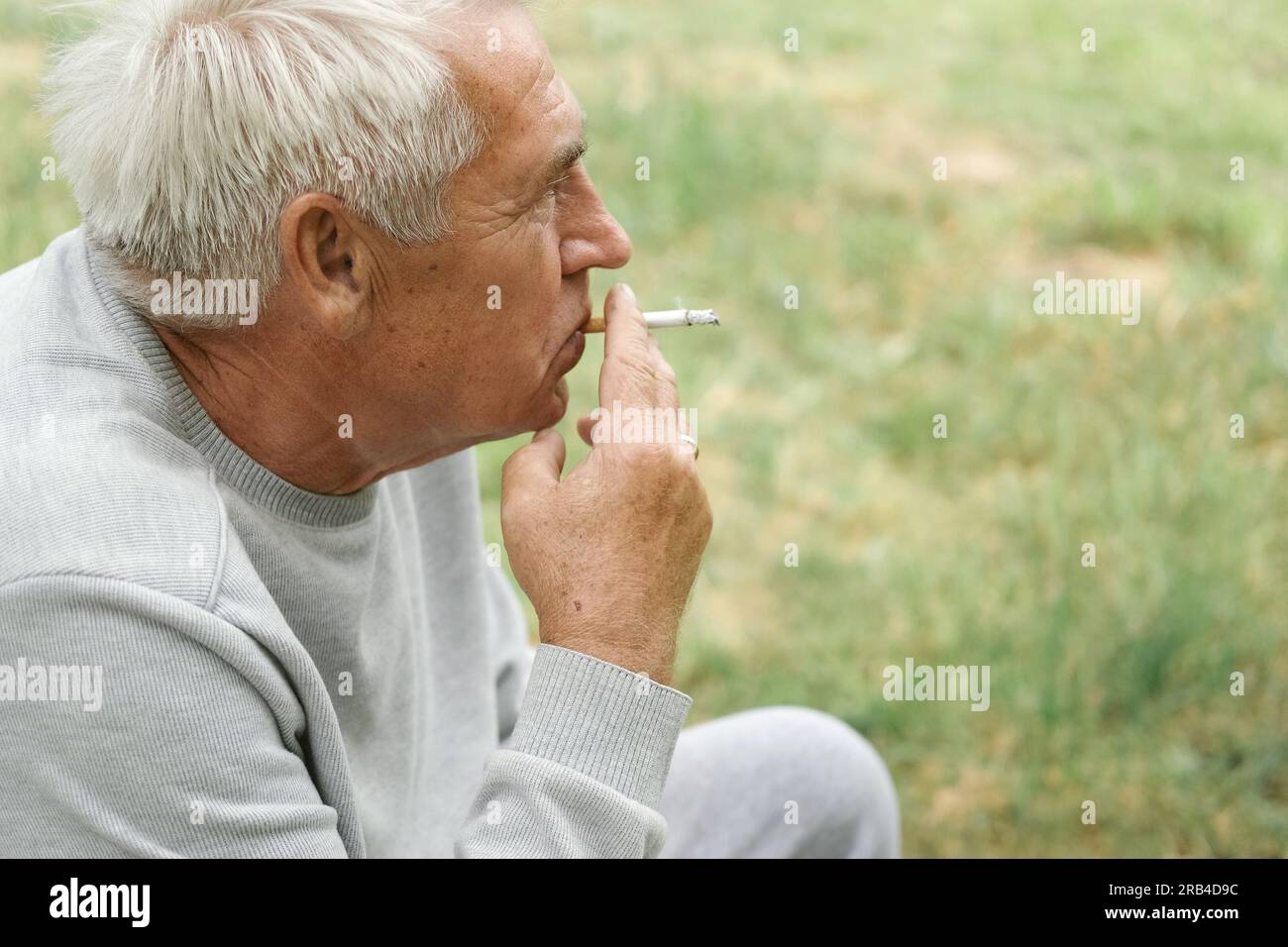 pension cigarette Senior man lighting up a cigarette outdoors against green nature  background. Old thoughtful man smoking, looking aside. Close Up Face.  Relaxed pension Stock Photo