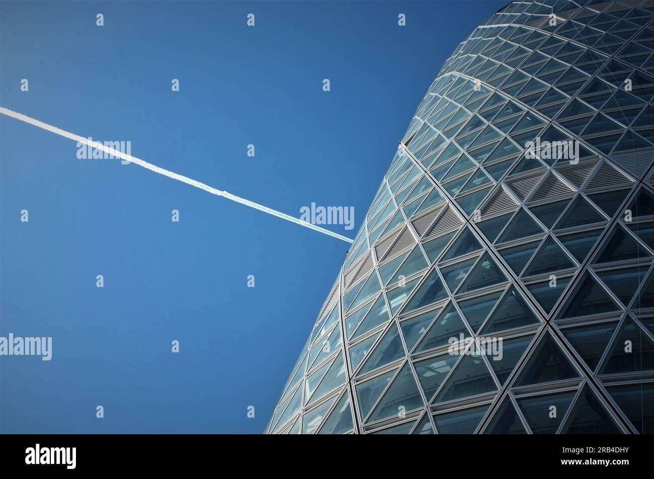 A chemtrail over a modern office building in Milan, Italy. Stock Photo