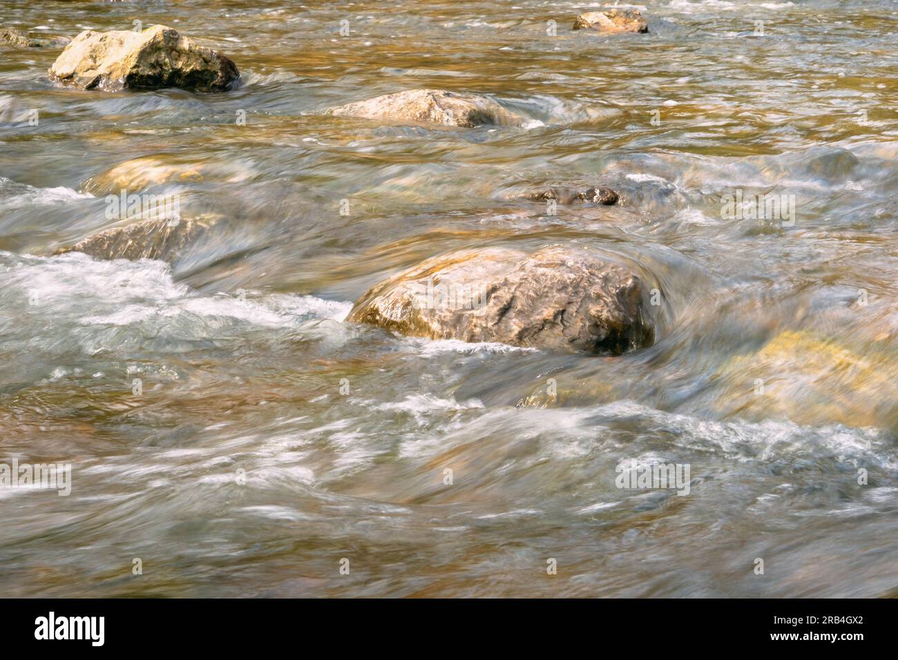Rapid and powerful water flow between large rocks, close-up 