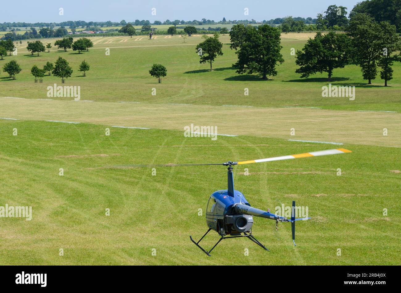 Robinson R-22 hovering low over grass airstrip at a wings and wheels event in the countryside at Heveningham Hall. Rural country in Suffolk. Parkland Stock Photo