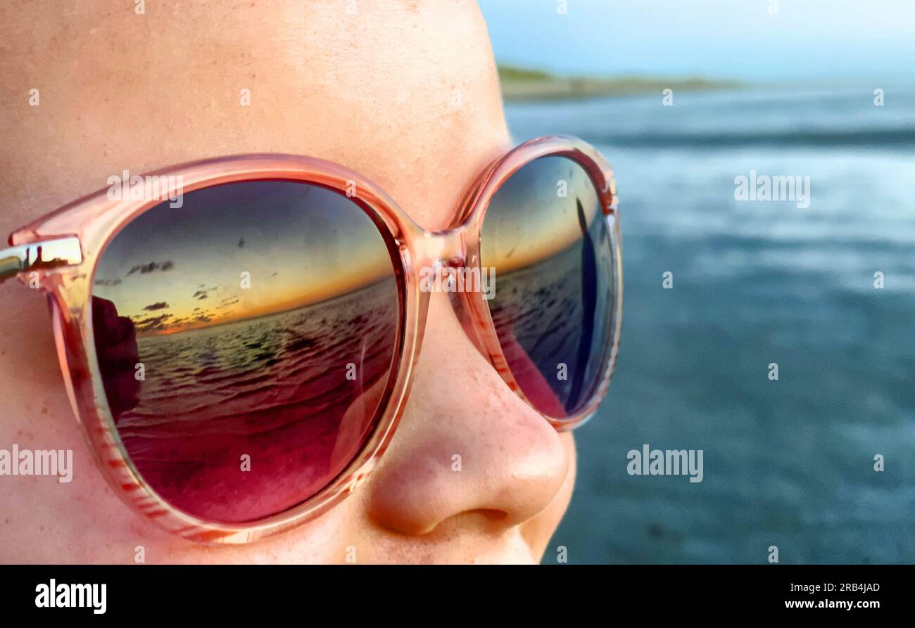 profile in sunglasses, reflection of the sunset in the sea in the glass of glasses, the concept of travel and summer vacation. High quality photo Stock Photo