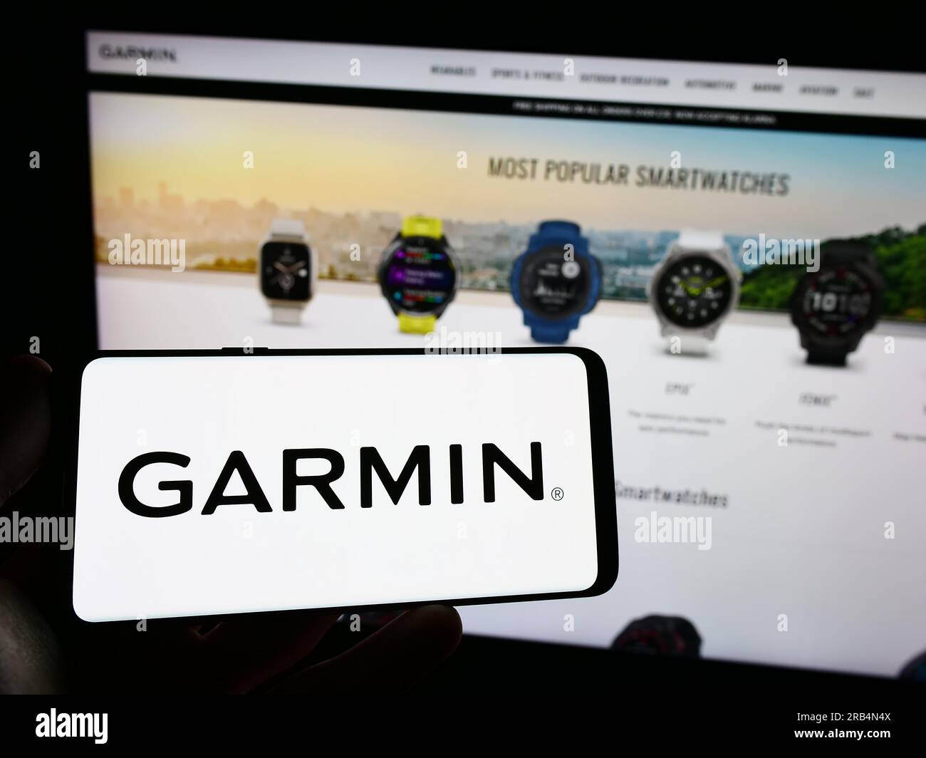 Person holding mobile phone with logo of technology company Garmin Ltd. on screen in front of business web page. Focus on phone display. Stock Photo