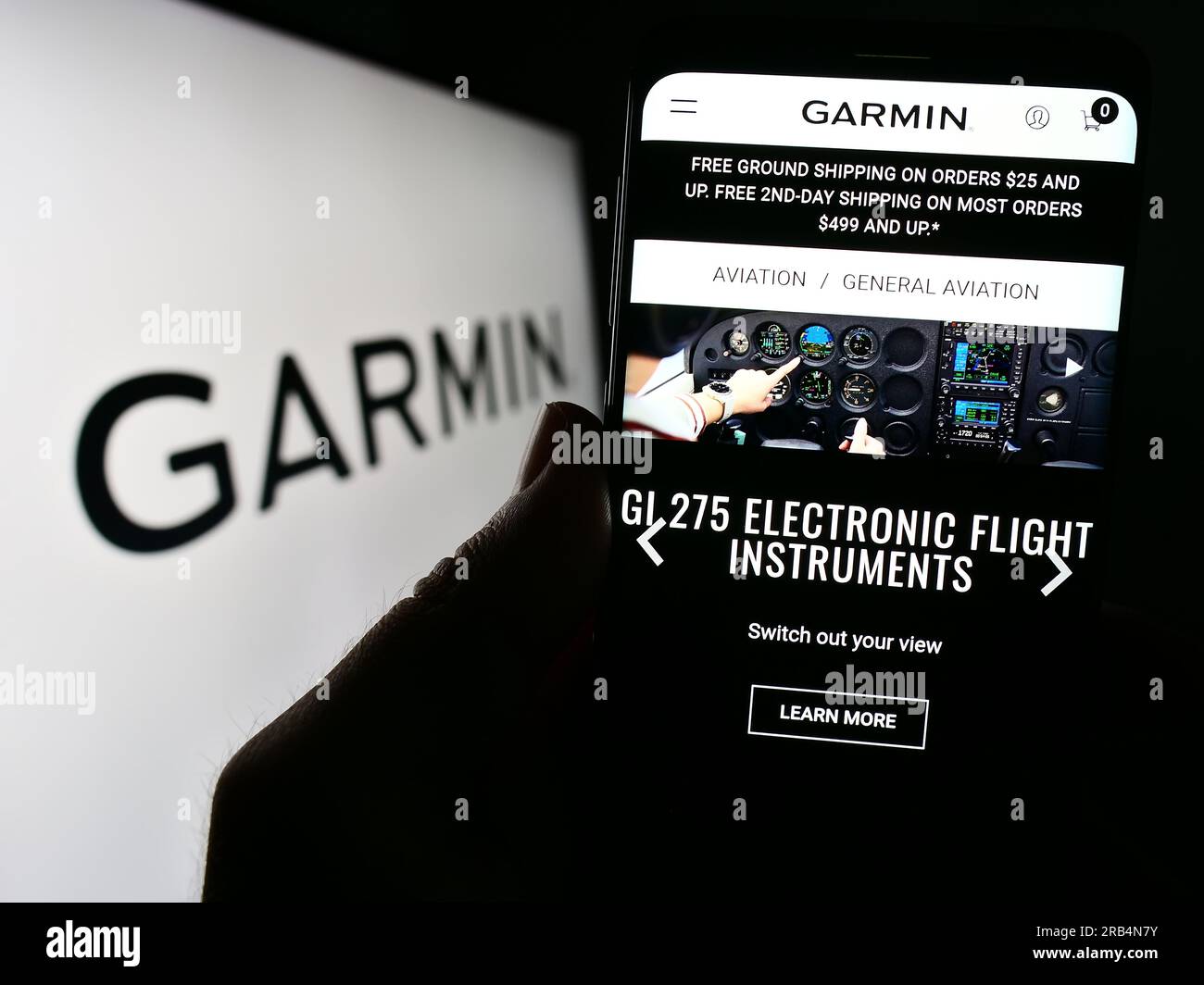 Person holding mobile phone with web page of technology company Garmin Ltd. on screen in front of logo. Focus on center of phone display. Stock Photo