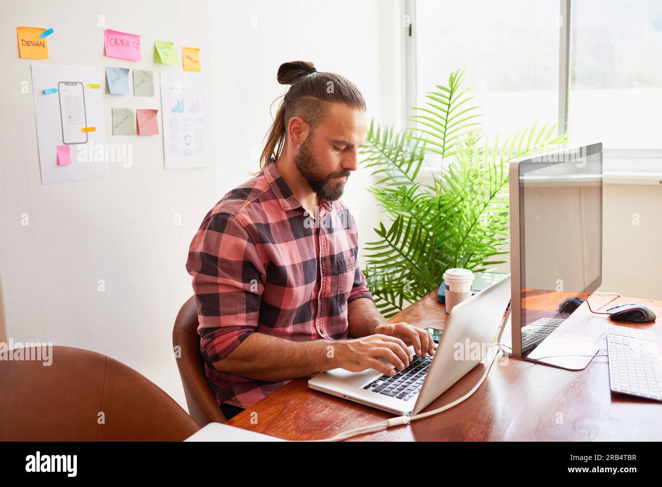 Senior developer works in open plan creative office, man bun hipster look Stock Photo