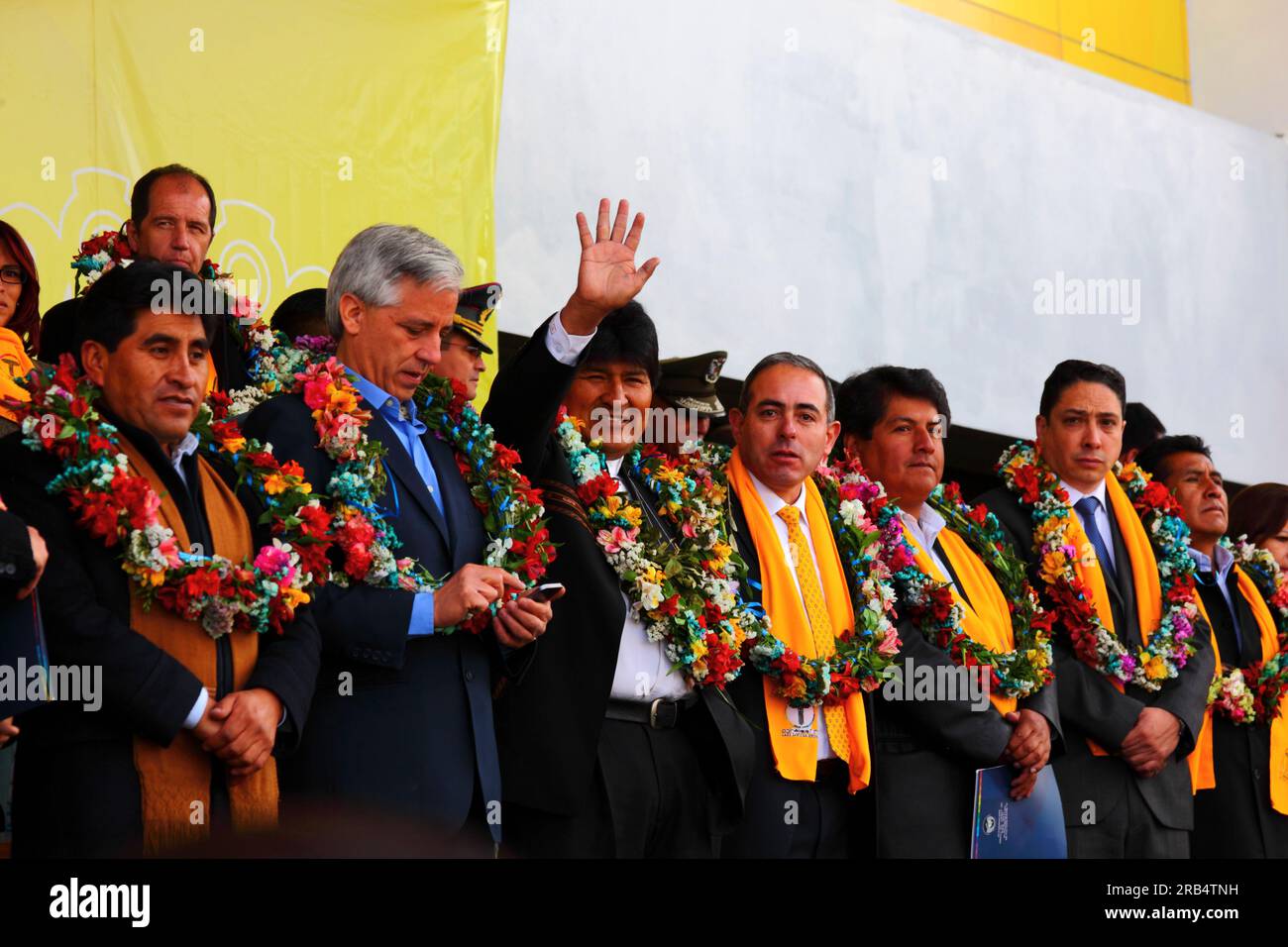 El Alto, Bolivia, 15th September 2014. Bolivian president Evo Morales (centre) waves to supporters during the inauguration ceremony of the cable car Yellow Line. Centre left is the vice president Alvaro Garcia Linera, far left the La Paz Department Governor Cesar Cocarico. The Yellow Line is the second of three cable car lines to be opened this year, and is part of an ambitious project to relieve traffic congestion. The first line opened in May, when all three are open they will be the world's longest urban cable car system. Stock Photo