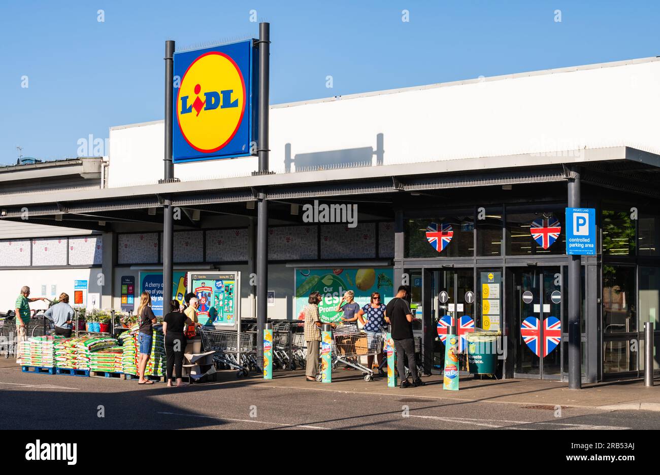 Line of people queueing outside a large Lidl food & grocery store or food retailer, waiting for it to open in Littlehampton, West Sussex, UK. Stock Photo