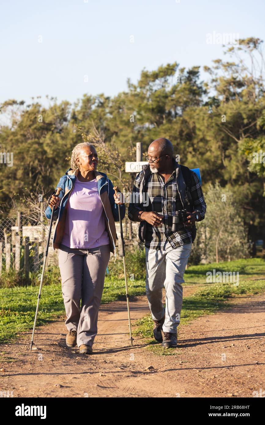 Senior african american couple with backpacks walking in sunny nature ...