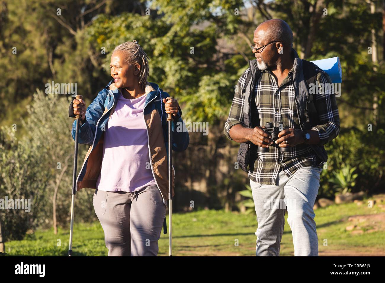 Senior african american couple with backpacks walking in sunny nature ...