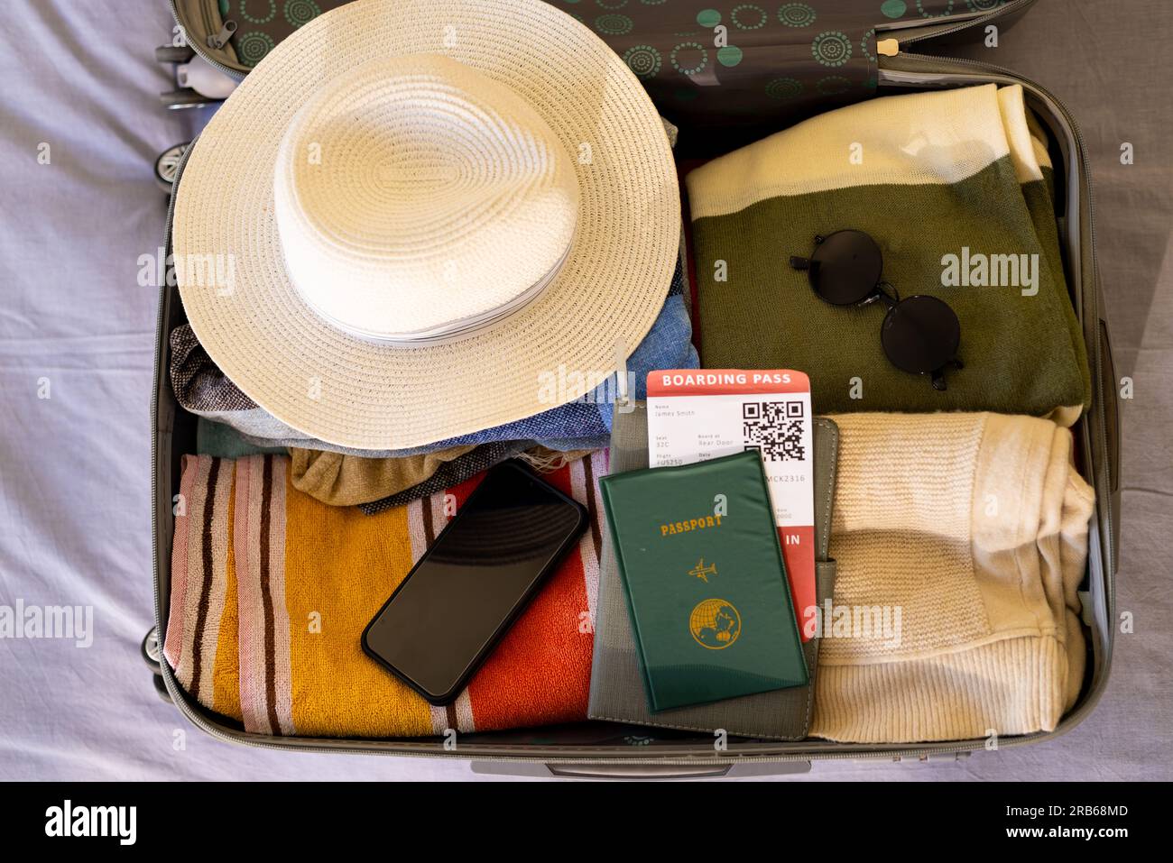 Overhead view of open suitcase with hat, clothes, smartphone, passport and ticket, on bed. Travel, vacations, preparation, communication, free time an Stock Photo