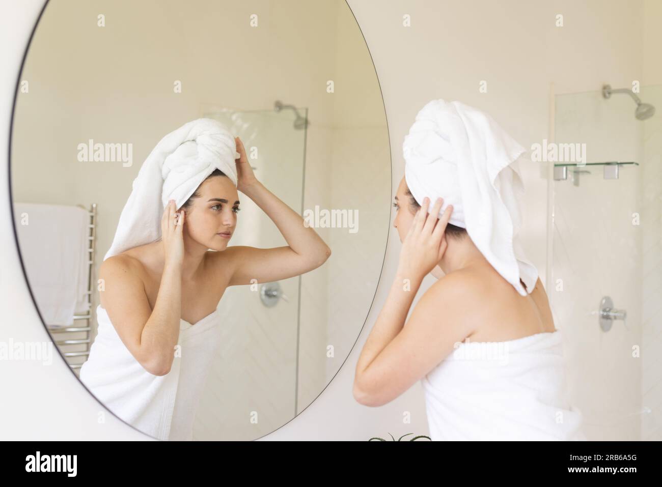 Caucasian woman with towel on head touching her face in bathroom. Domestic life, selfcare and lifestyle, unaltered. Stock Photo